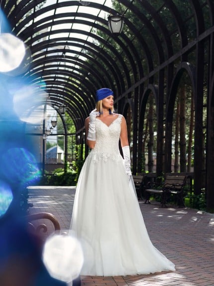 Булка в макси сватбена рокля големи размери седи на пейка в очарователен оранжериен тунел