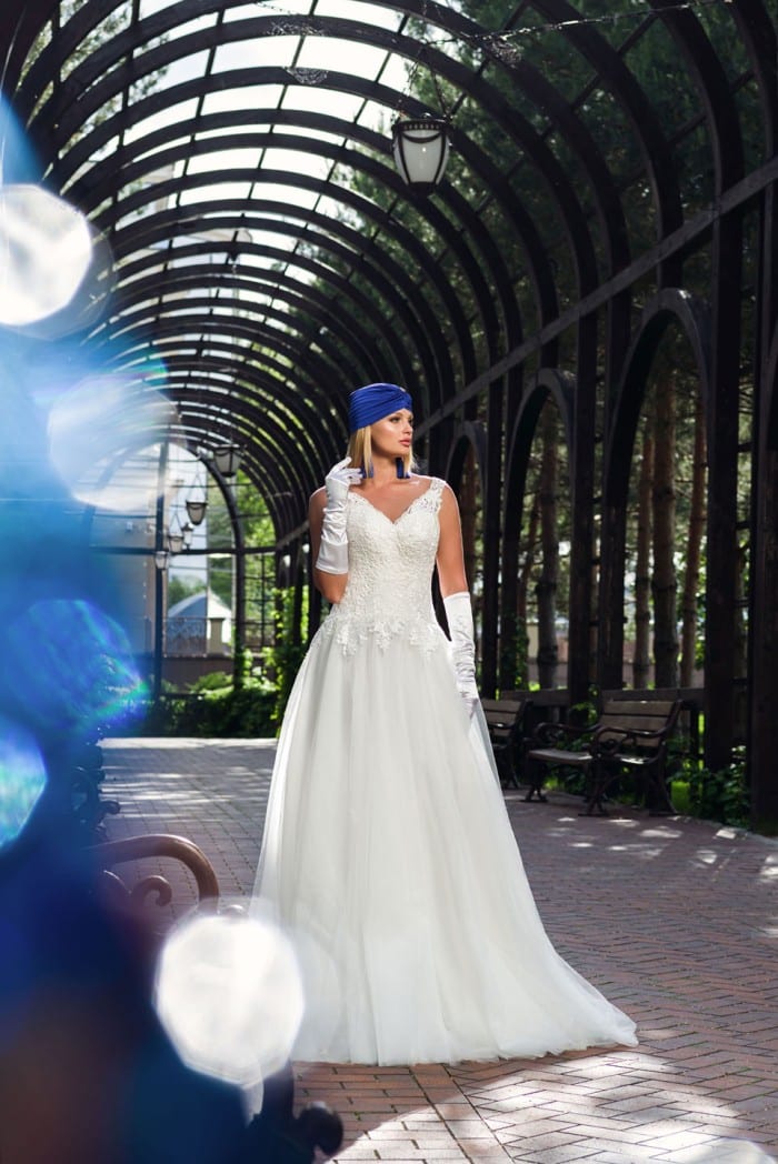 Булка в макси сватбена рокля големи размери седи на пейка в очарователен оранжериен тунел
