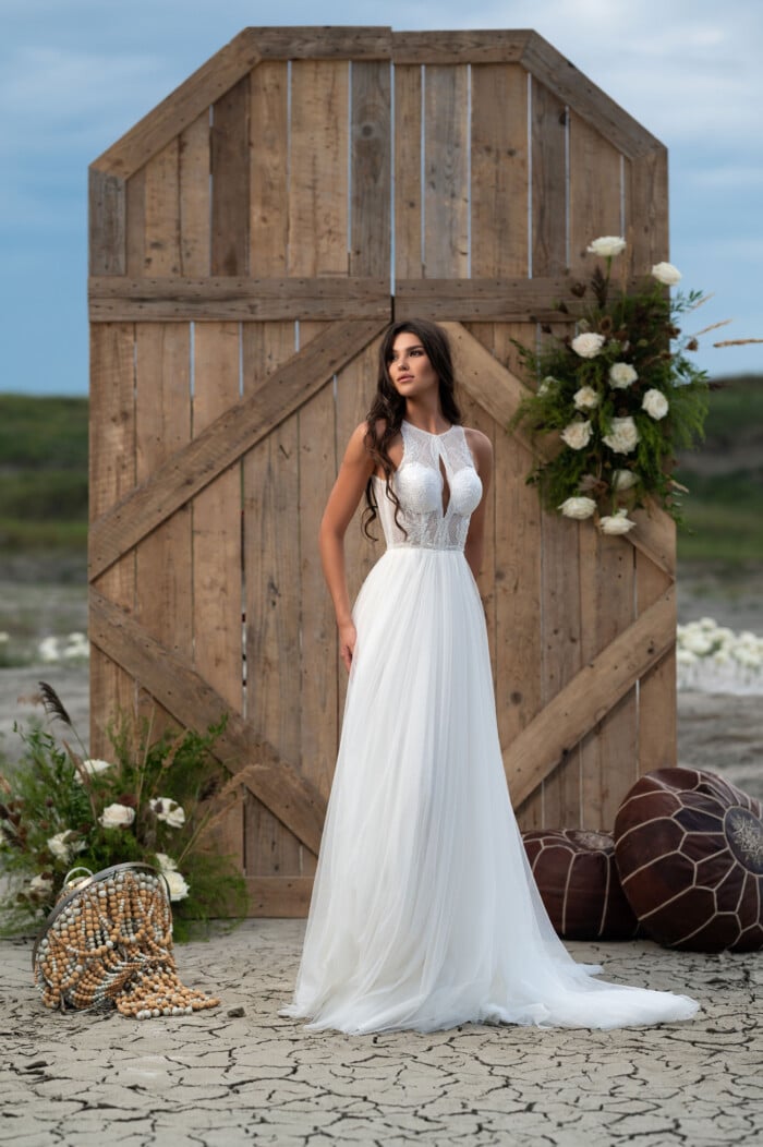 Модел с булчинска рокля А-линия с фин тюл и елегантна дантела, позира пред бели рози
