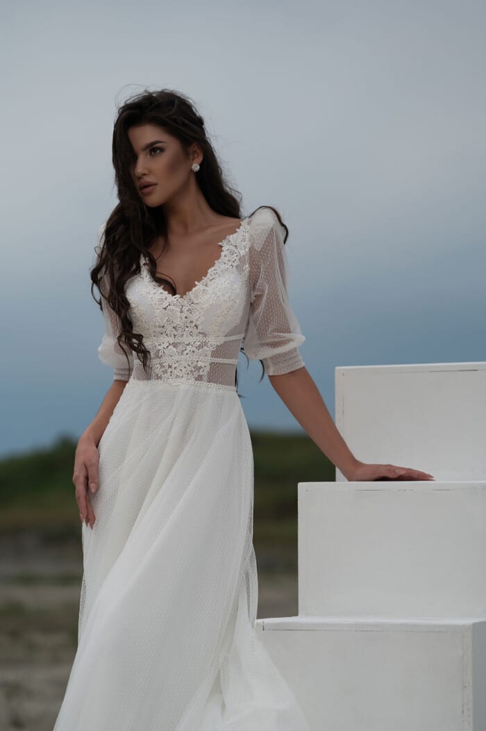 Модел позира с 2024 булчинска рокля с дълбоко деколте Люсил, показваща изящна дантела и елегантни детайли