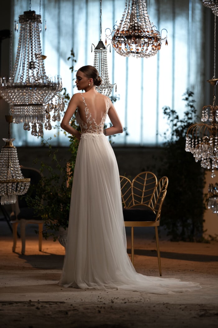 Булчинска рокля модел Мади, с изящни цветни апликации и дантелени ръкави, представена в луксозен салон с кристални плилеи.