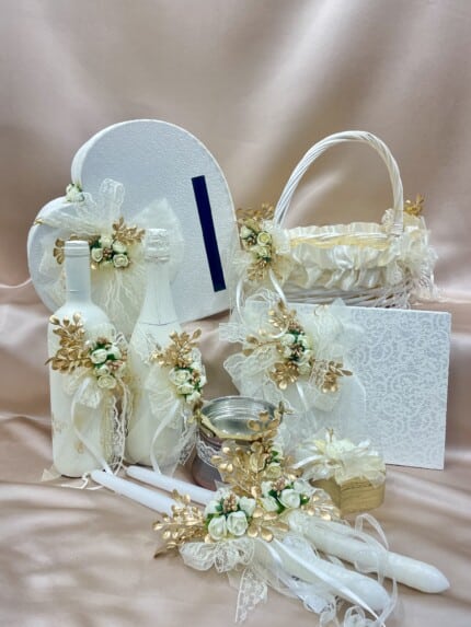 Елегантни сватбени аксесоари комплект с бяло и златно, включващ кутия за пари и ритуални свещи, на фон на шампанско плат