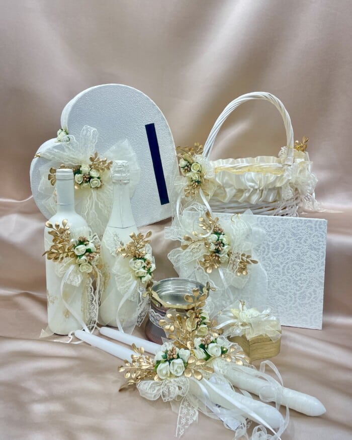 Елегантни сватбени аксесоари комплект с бяло и златно, включващ кутия за пари и ритуални свещи, на фон на шампанско плат