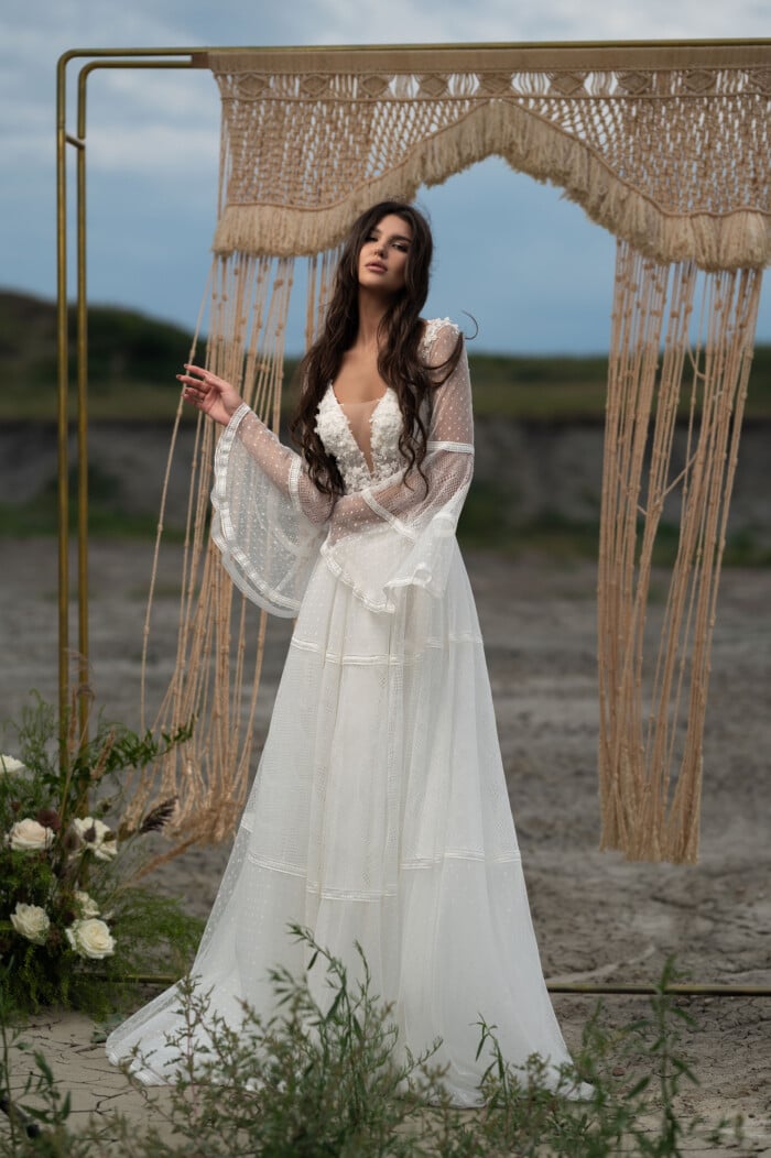 Винтидж сватбена рокля Никита с бохо стил и дълги ръкави, позиционирана на плаж пред сватбен балдахин.