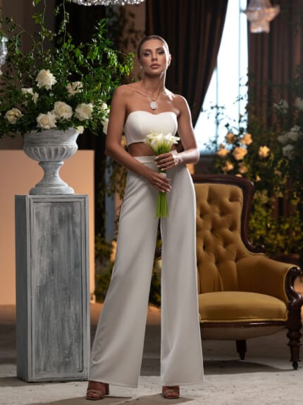 Модерен дамски сватбен костюм с панталон, показан от елегантна билка в луксозен интериор.