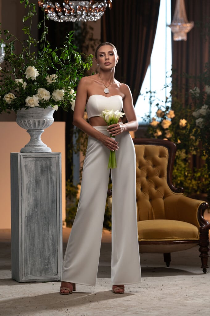 Модерен дамски сватбен костюм с панталон, показан от елегантна билка в луксозен интериор.