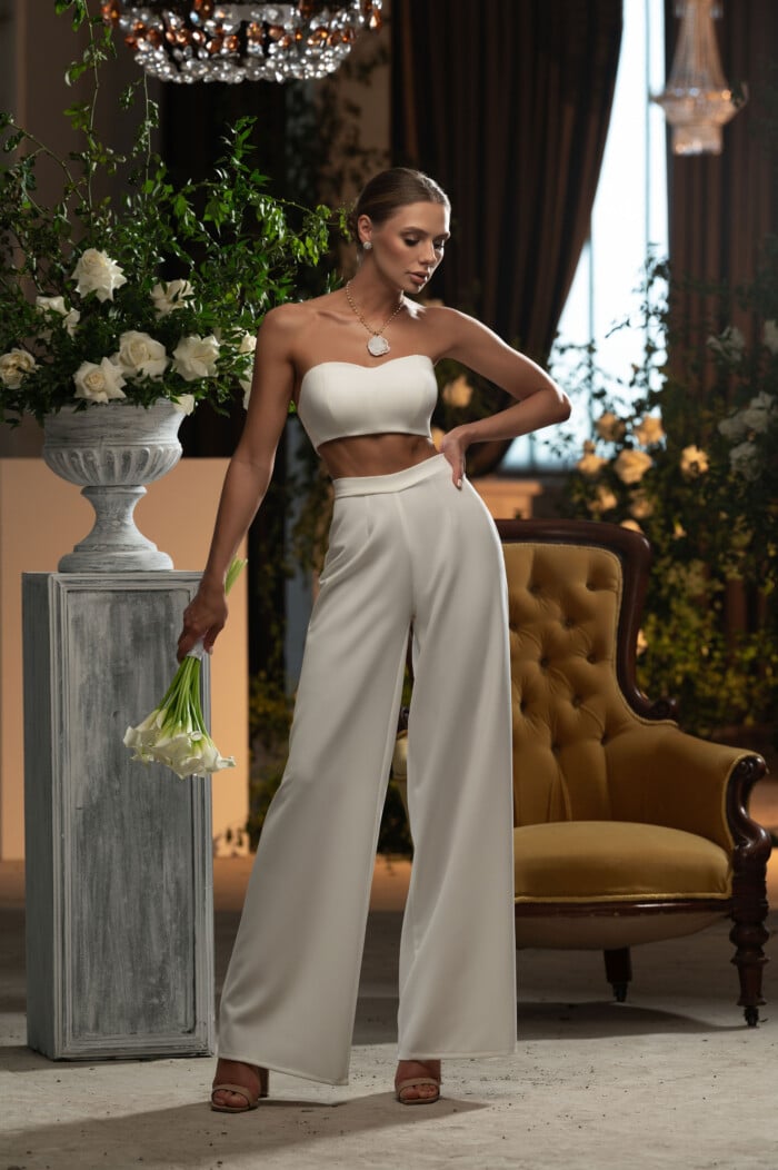 Модерен сватбен костюм с панталон, показан от елегантна билка в луксозен интериор.