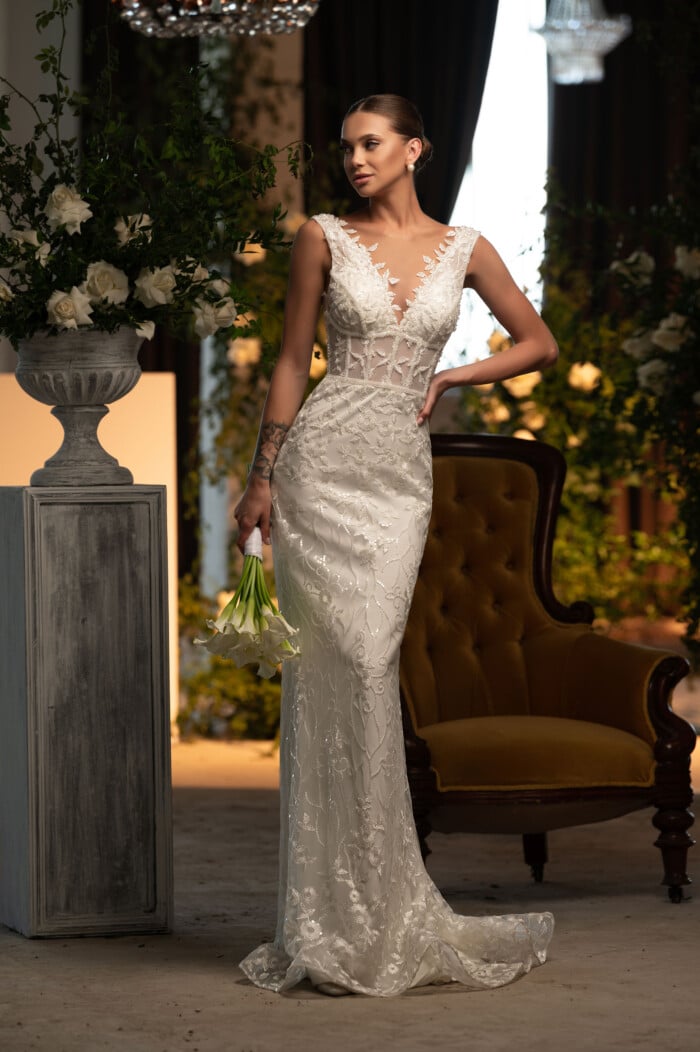 Модел със сватбена рокля русалка Саманта с ръчна бродерия и луксозни материи, позирана в елегантна обстановка.