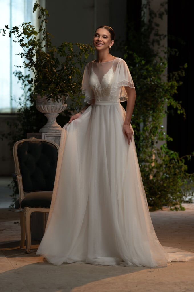 Елегантна сватбена рокля с шифонови ръкави и изящен отворен гръб, изложена в сватбен център.